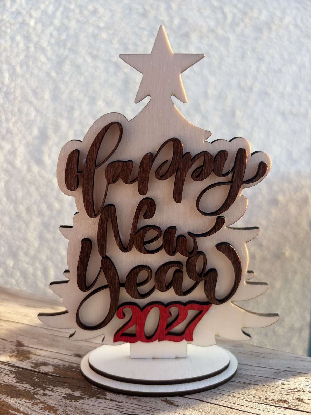 Árbol de Navidad de madera de abedul con la frase Happy New Year calada en relieve y el año 2027 en rojo, sobre una base redonda