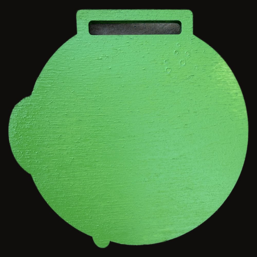 Capa trasera de la medalla de madera pintada de verde, con el mismo contorno troquelado y la ranura de la cinta cortada en la misma posicion