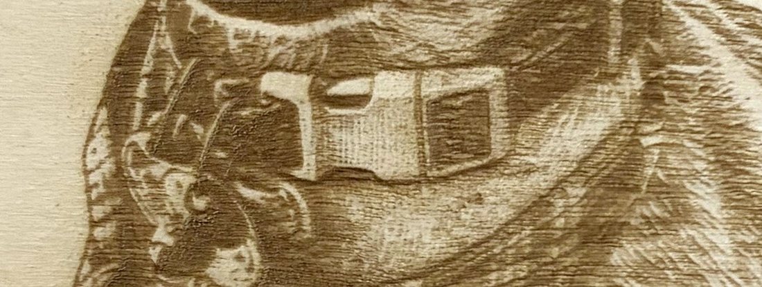 Detalle del collar grabado en madera: la hebilla de clic, el tejido de la cincha y las chapas colgando